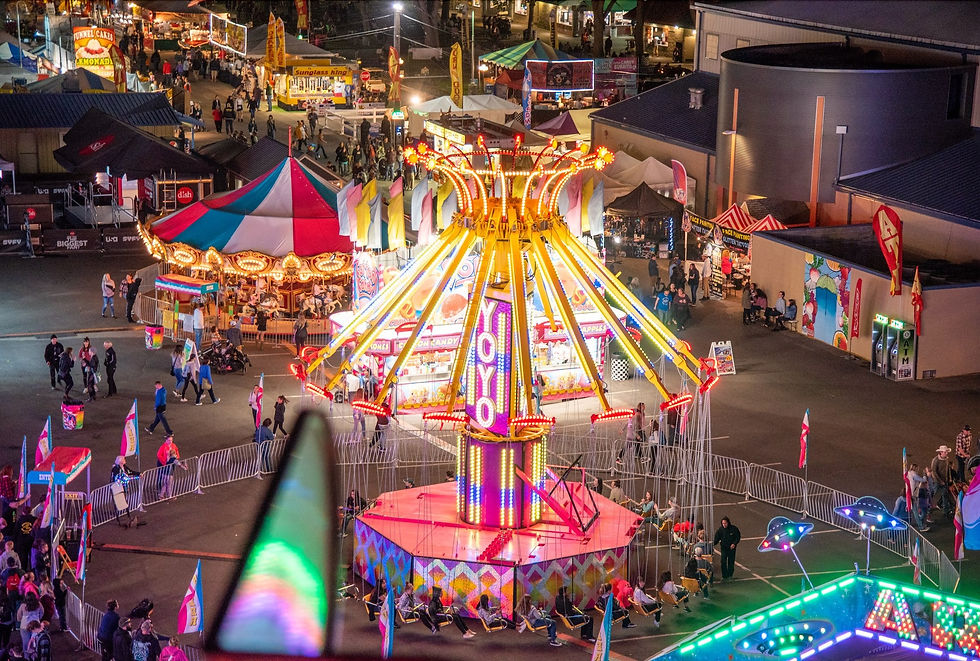A vibrant carnival scene at night with a brightly lit Yo-Yo ride, carousel, and concession stands. People walk around, enjoying the lively atmosphere.
