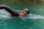Swimmer in black wetsuit and goggles doing freestyle in clear turquoise water.