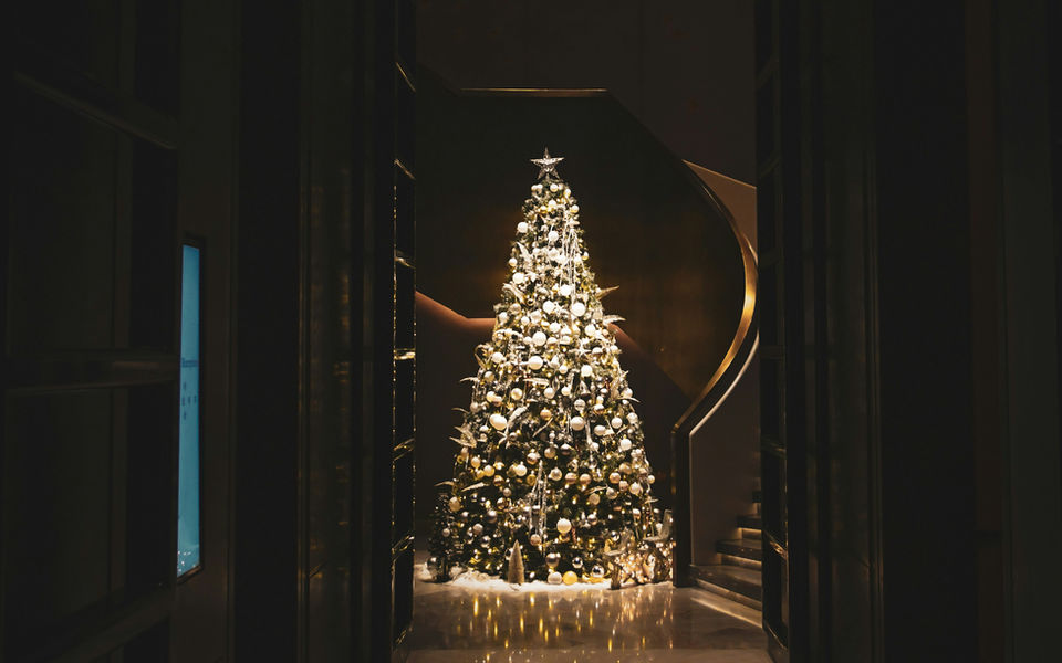A glowing Christmas tree at the end of a dark, paneled hallway