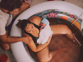 Labouring woman in an inflatable birth pool at home while partner provides hands-on support.
