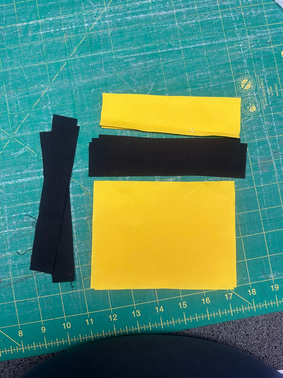 Yellow and black fabric strips on a green cutting mat with measurement markings. Text on mat includes ruler units. Crafting setup.