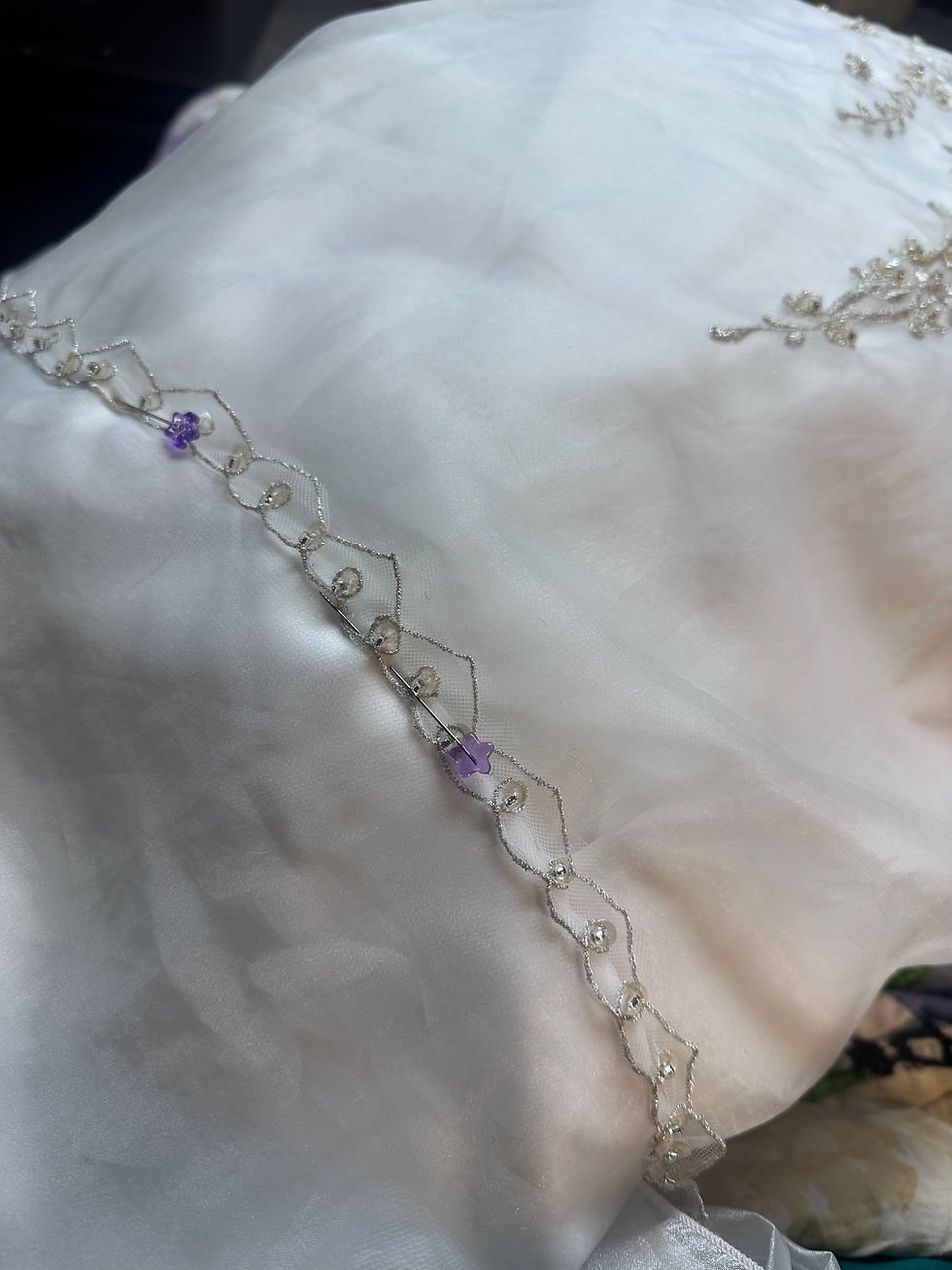 White fabric with delicate embroidery, featuring a purple flower bead and pearl accents. Soft lighting creates an elegant, serene mood.
