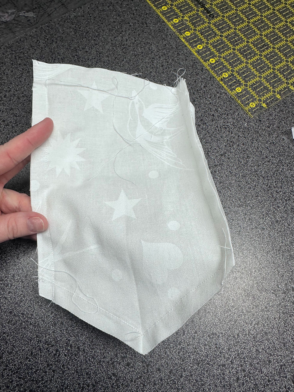 Fingers hold white fabric with star and flower patterns on a speckled surface. A measurement grid is partially visible in the background.