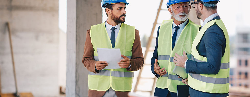 Three men wearing safety vests and hard hats engaged in conversation at a construction site