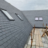 A sloped roof with grey slate tiles, featuring skylights, and scaffolding along the edge