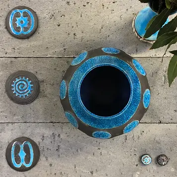 A blue vase holds a single flower, surrounded by colorful buttons on a light surface