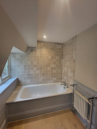 A bathroom featuring a white bathtub, tiled walls with a mix of light-coloured tiles, and a towel radiator