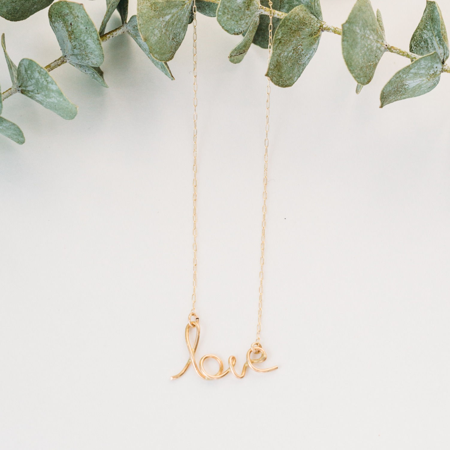 Gold Love necklace on greenery