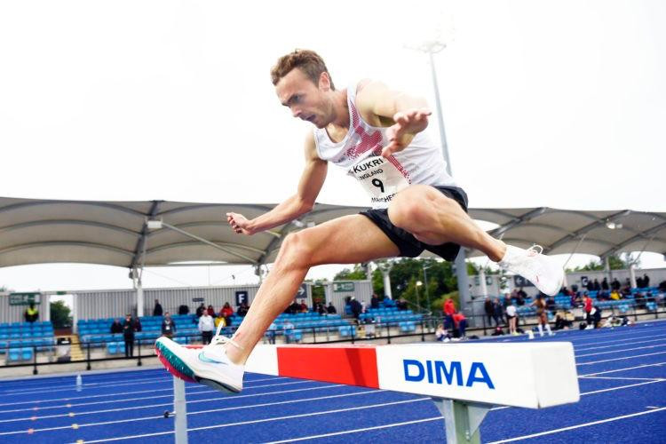 Athlete Will Battershill jumps over a steeplechase barrier on an athletics track at the Manchester International