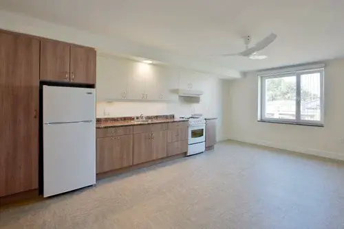 Apartment kitchen with freshly painted light walls, wood cabinets, white appliances, large window, and bright ceiling lights.