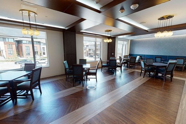 Greystone Village Retirement dining room with freshly painted light walls, decorative ceiling panels, pendant lighting, dining tables, blue accent wall, and wood flooring.