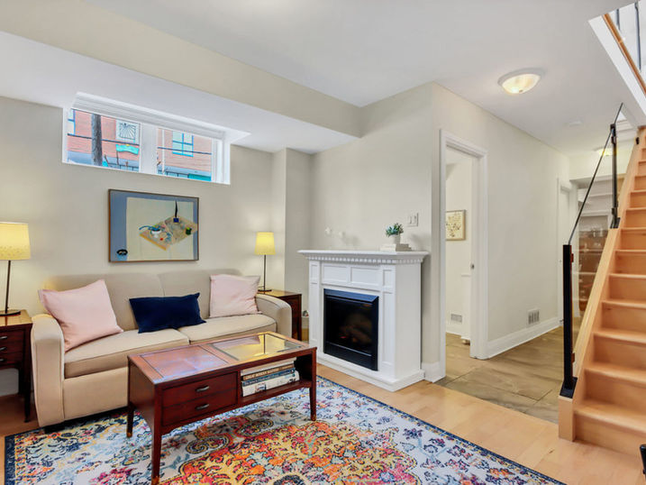 Ravenhill Common living room with freshly painted light walls, fireplace, staircase, sofa, coffee table, colourful rug, and wood flooring.
