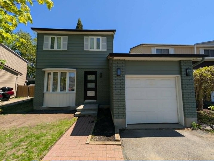 Front view of a two-storey house with freshly painted green siding and brick, white shutters and trim, black front door, white garage door, and updated exterior finishes.