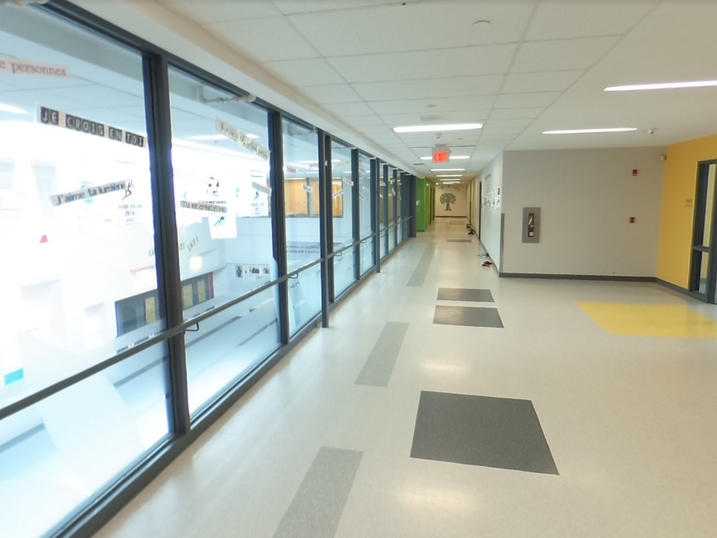 École Élémentaire Catholique Jean-Robert-Gauthier corridor with freshly painted light walls, glass partitions, yellow accent doors, grey floor details, and bright ceiling lights.
