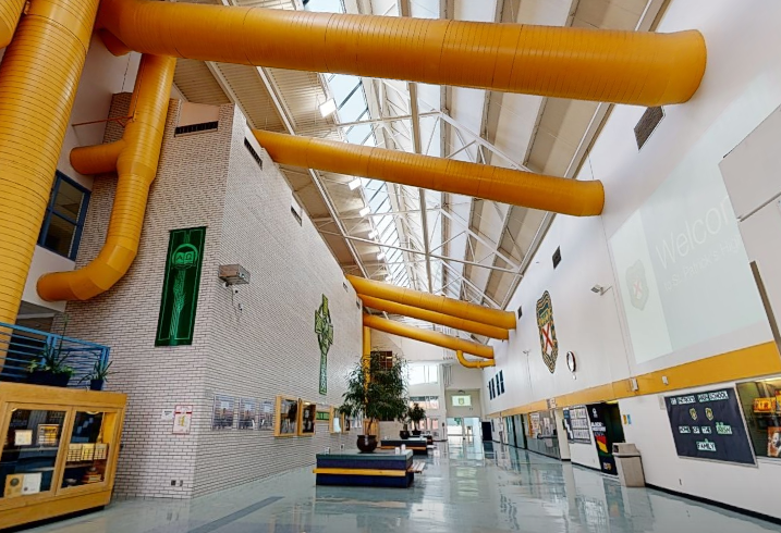 St. Patrick’s High School atrium with freshly painted white walls, yellow overhead structural beams, skylight, display areas, green accent details, and polished school flooring.