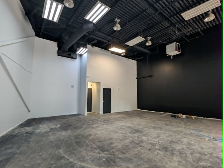 Completed commercial studio painting at Wellspring Studios in Nepean, Ontario, showing an open warehouse space with black painted exposed ceiling, black feature wall, white walls, dark doors, ductwork, lighting and concrete floor.