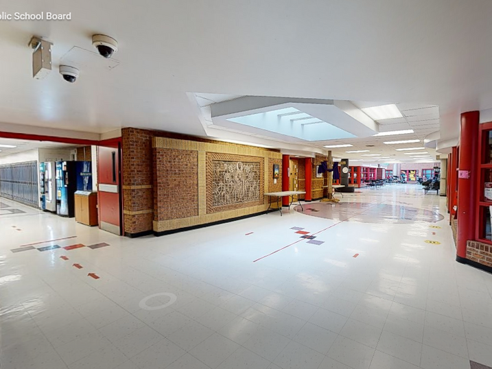 St. Mark Catholic School corridor with freshly painted light walls, red accent details, brick feature walls, display areas, skylights, and polished school flooring.