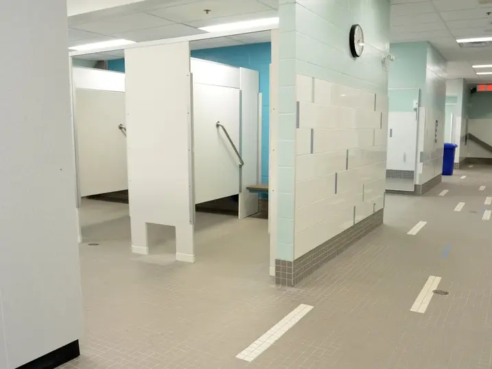 Francois Dupuis Recreation Centre locker room area with freshly painted light block walls, blue accent sections, tiled floors, changing stalls, and bright ceiling lights.