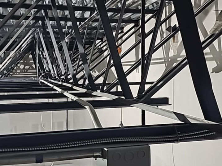 Riverside South Secondary School interior with dark painted structural steel beams, exposed roof framing, white walls, and visible ceiling equipment.