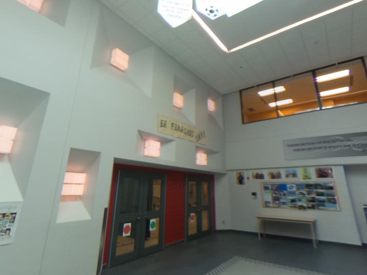 École Élémentaire Catholique Jean-Robert-Gauthier atrium with freshly painted light walls, recessed wall openings, skylight, interior windows, entrance doors, and school display area.