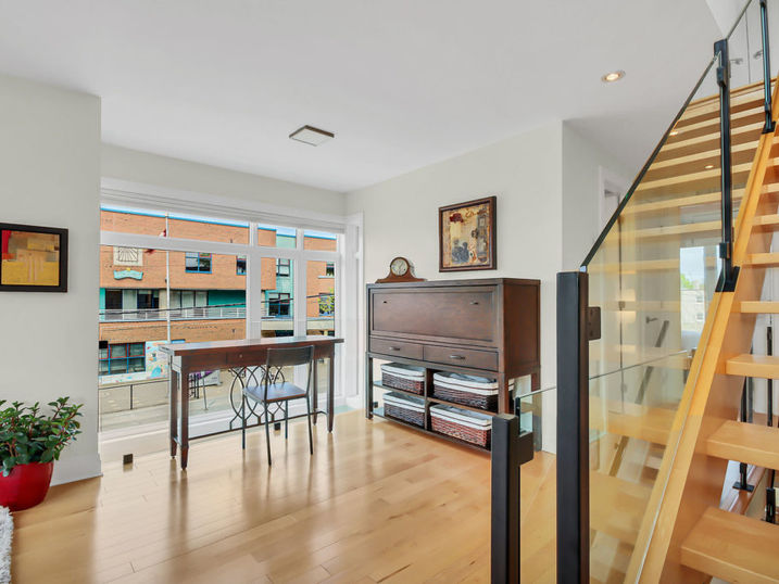 Ravenhill Common living area with freshly painted light walls, wood staircase, large windows, dining area, piano, and light wood flooring.