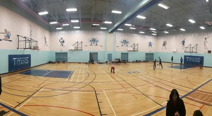 Mother Theresa High School gymnasium with freshly painted steel deck ceiling, blue and grey walls, basketball court lines, school graphics, wall padding, and bright overhead lighting.