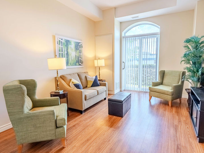 Wildpine Retirement Residence living room with freshly painted light walls, sofa, armchairs, wood flooring, arched balcony door, lamps, and warm residential finishes.