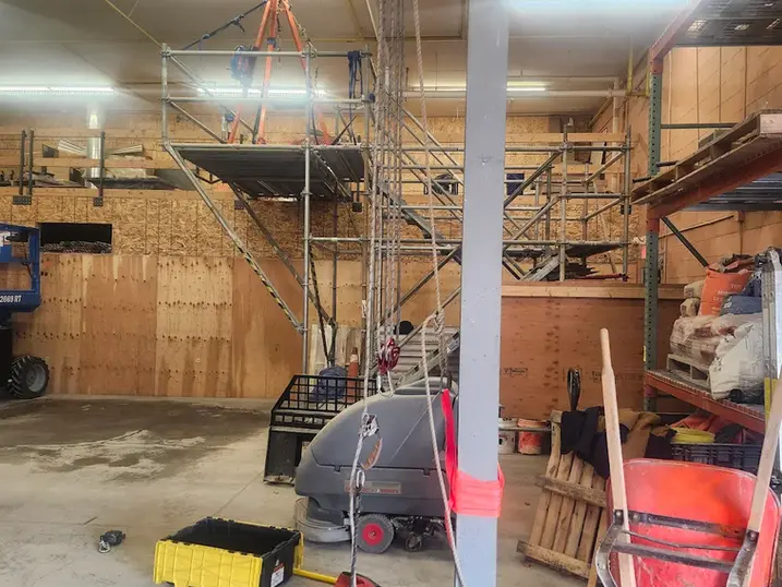 LiUNA Local 527 training workshop with scaffolding, safety equipment, painted structural column, plywood walls, concrete floor, and hands-on construction training setup.
