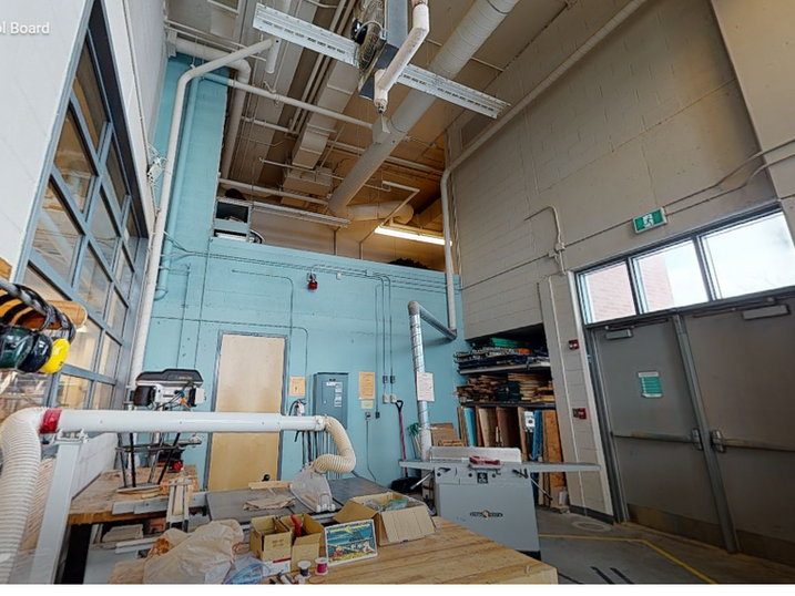 St. Francis Xavier Catholic High School technical classroom with freshly painted blue block walls, exposed ceiling structure, ductwork, equipment, worktables, and high wall surfaces.