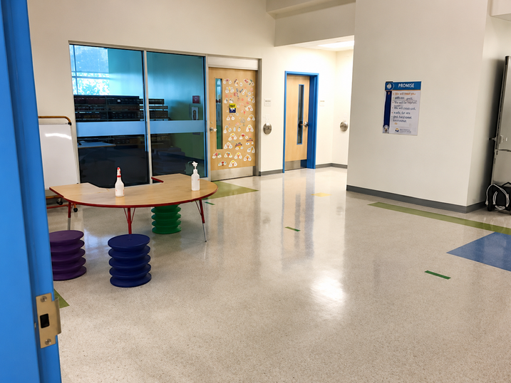Horizon Jeunesse Elementary School common area with freshly painted light walls, blue door frames, glass partitions, colourful seating, and polished flooring.