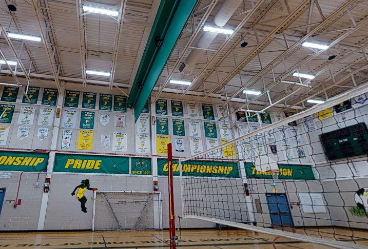 St. Patrick’s High School gymnasium with freshly painted steel deck ceiling, green and yellow wall accents, volleyball net, school banners, wall padding, and bright overhead lighting.
