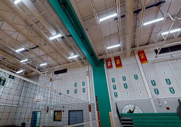 St. Patrick’s High School gymnasium with freshly painted steel deck ceiling, high white walls, green accent column, volleyball net, school banners, and bright overhead lighting.