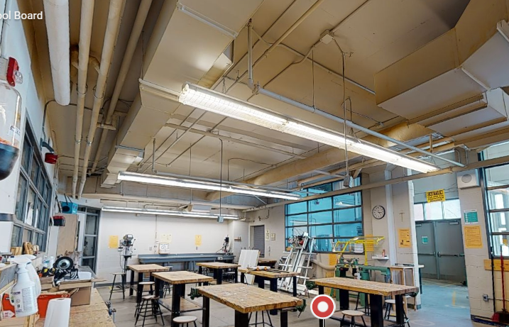 St. Francis Xavier Catholic High School wood shop with freshly painted high walls, exposed ceiling structure, worktables, tools, tall windows, and technical classroom equipment.