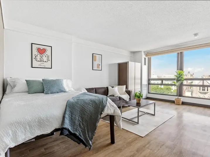 111 Cooper Street student suite with freshly painted white walls, bed, sofa, large window, wood flooring, and modern residential furnishings.