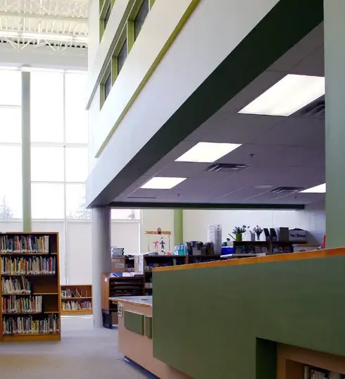 Stittsville Elementary School library with colourful painted green and yellow walls, high windows, bookshelves, reception desk, and detailed multi-level architectural finishes.