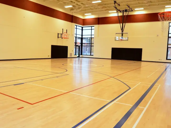 Overbrook Community Centre gymnasium with freshly painted light walls, warm accent band, basketball hoops, wall padding, wood sports flooring, and bright ceiling lights.