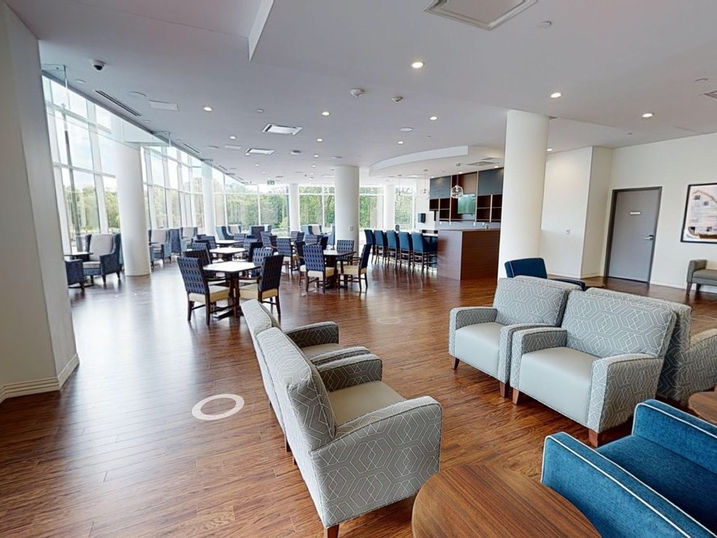 Greystone Village Retirement common area with freshly painted light walls, white columns, lounge seating, dining tables, wood flooring, and large windows with natural light.