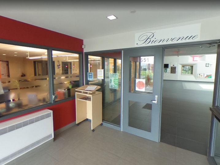 École Élémentaire Catholique Jean-Robert-Gauthier entrance with freshly painted light walls, red accent wall, glass doors, painted frames, reception window, and welcome signage.