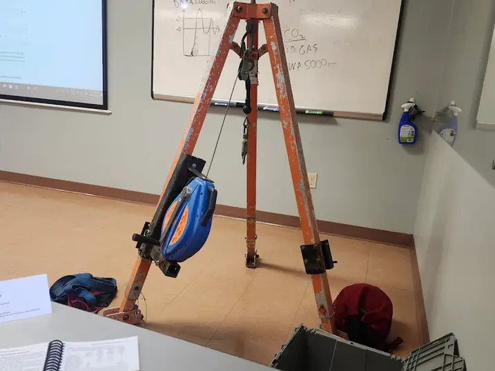 LiUNA Local 527 training classroom with freshly painted light walls, training tripod equipment, whiteboard, projector screen, desks, and safety gear.