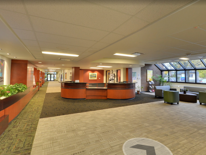 Overbrook Community Centre lobby with freshly painted warm accent walls, reception desk, seating area, plants, carpet flooring, large windows, and bright public circulation space.