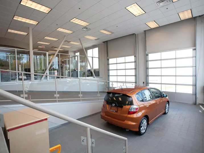 Hunt Club Honda service bay with freshly painted light walls, orange vehicle, glass partitions, overhead doors, tiled flooring, and bright ceiling lights.
