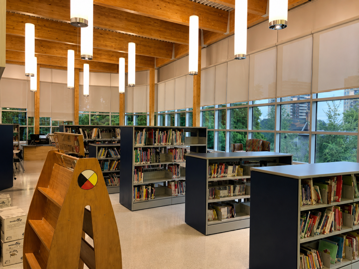 Horizon Jeunesse Elementary School library with freshly painted light walls, tall windows, bookshelves, wood ceiling, hanging lights, and bright natural light.
