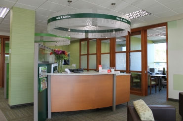 TD Canada Trust banking service area with freshly painted green accent walls, service counter, wood office partitions, circular overhead signage, and bright ceiling lights.