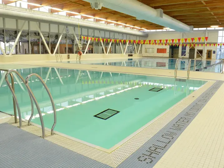Francois Dupuis Recreation Centre indoor pool with stained wood ceiling, painted structural beams, swimming lanes, tile deck, and bright overhead lighting.