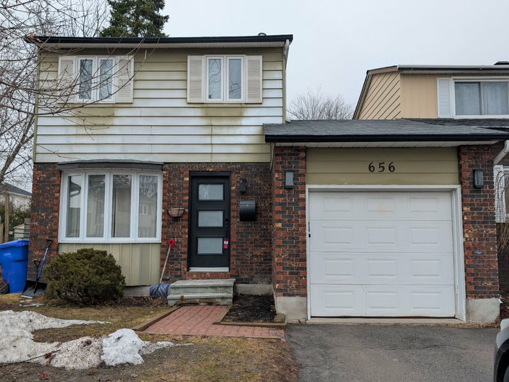 Before view of a two-storey brick and siding house with white garage door, front entrance, shutters, and original exterior finishes before painting.