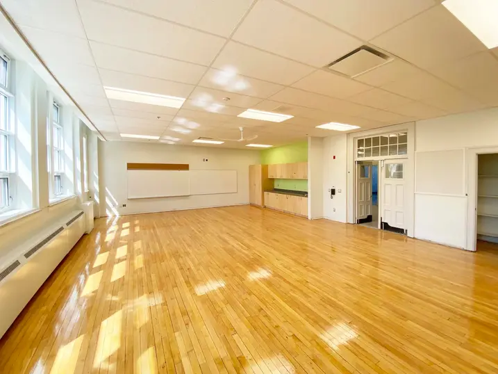 Elmdale Public School multi-purpose room with freshly painted light walls, large windows, wood flooring, green accent cabinets, and bright ceiling lights.