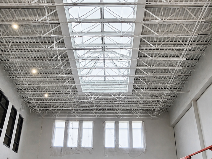 After view of Riverside South Secondary School with freshly painted white steel deck ceiling, skylight, exposed roof structure, tall windows, and bright interior space.