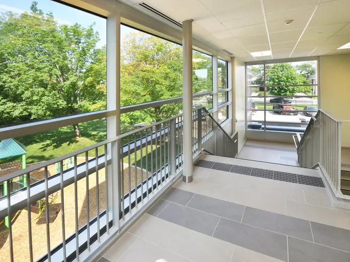 Elmdale Public School stairwell landing with freshly painted light walls, painted window frames, metal railings, large windows, grey tile flooring, and bright natural light.