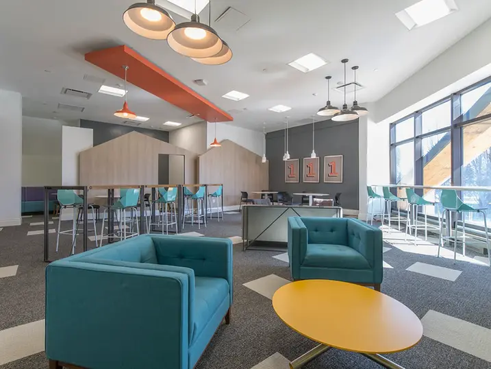 111 Cooper Street student lounge with freshly painted accent ceiling, teal lounge chairs, yellow table, study bar, large windows, patterned carpet, and bright ceiling lights.