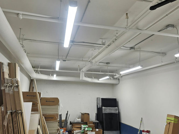 Salus Capilano service room with freshly painted exposed ceiling, concrete walls, fluorescent lighting, visible pipes, and storage materials.